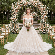 A bride posing in a wedding venue archway wearing a sexy, backless A-line wedding dress with delicate lace appliques and a tulle skirt.