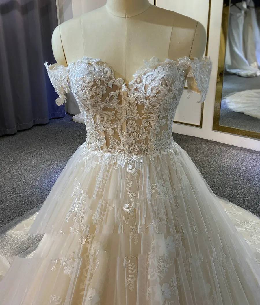 Close-up detail of a bridal dress bodice showing the intricate white floral lace embroidery and sweetheart neckline over a nude illusion base.