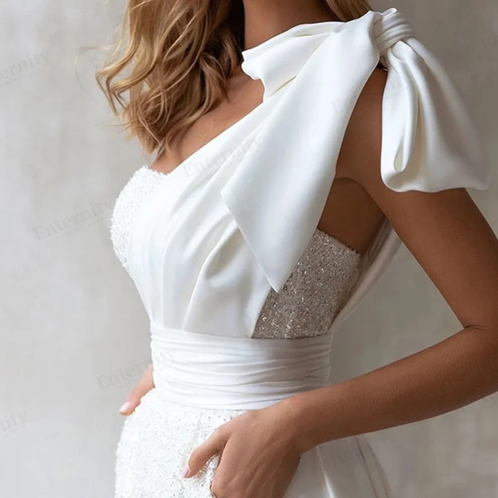 Macro crop of a modern wedding reception jumpsuit showing the contrasting textures between the smooth pleated satin shoulder strap and the shimmering sequined bodice.