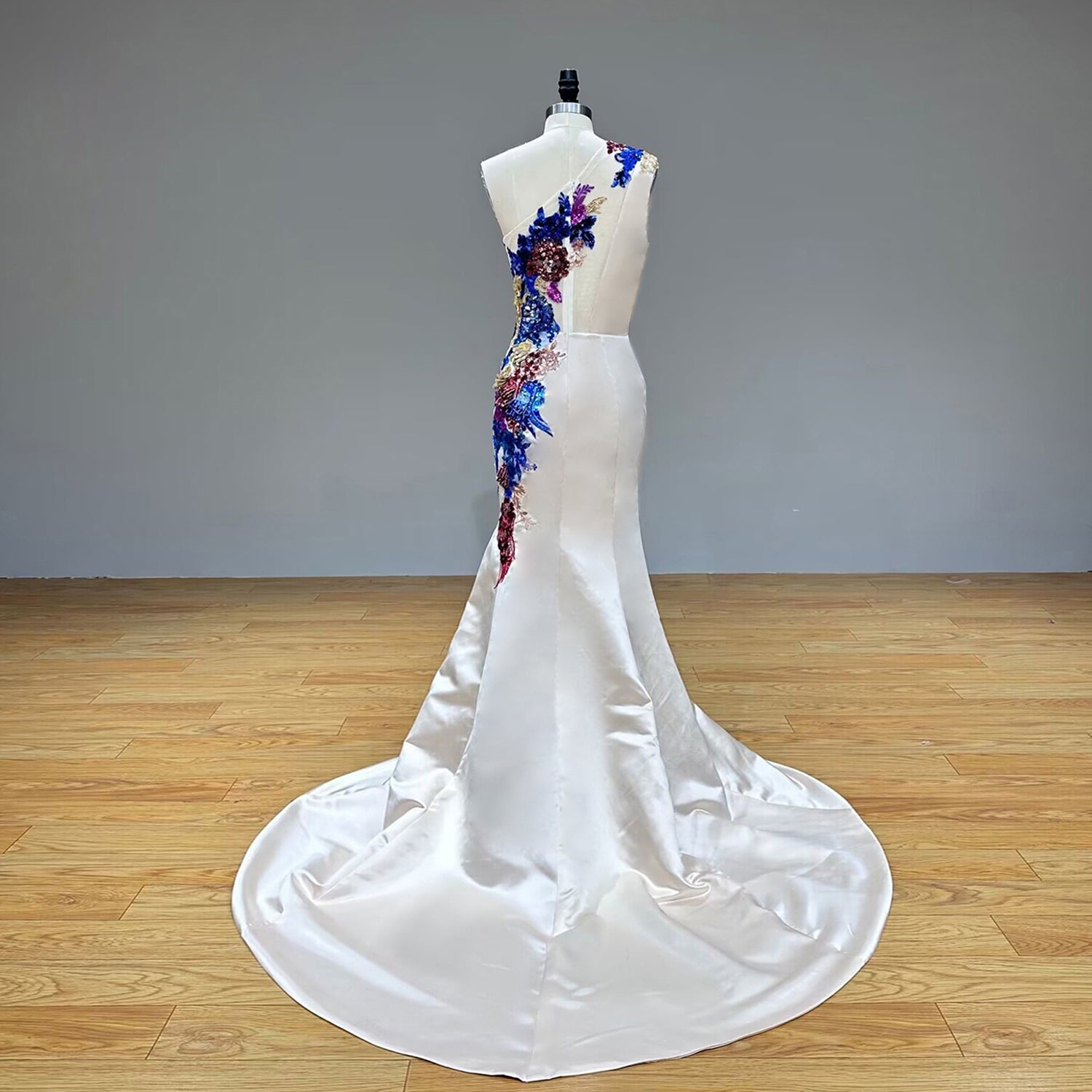 Full-length back studio view of a luxury one-shoulder evening gown showing the smooth, clean pool of the elegant floor-length sweep train.