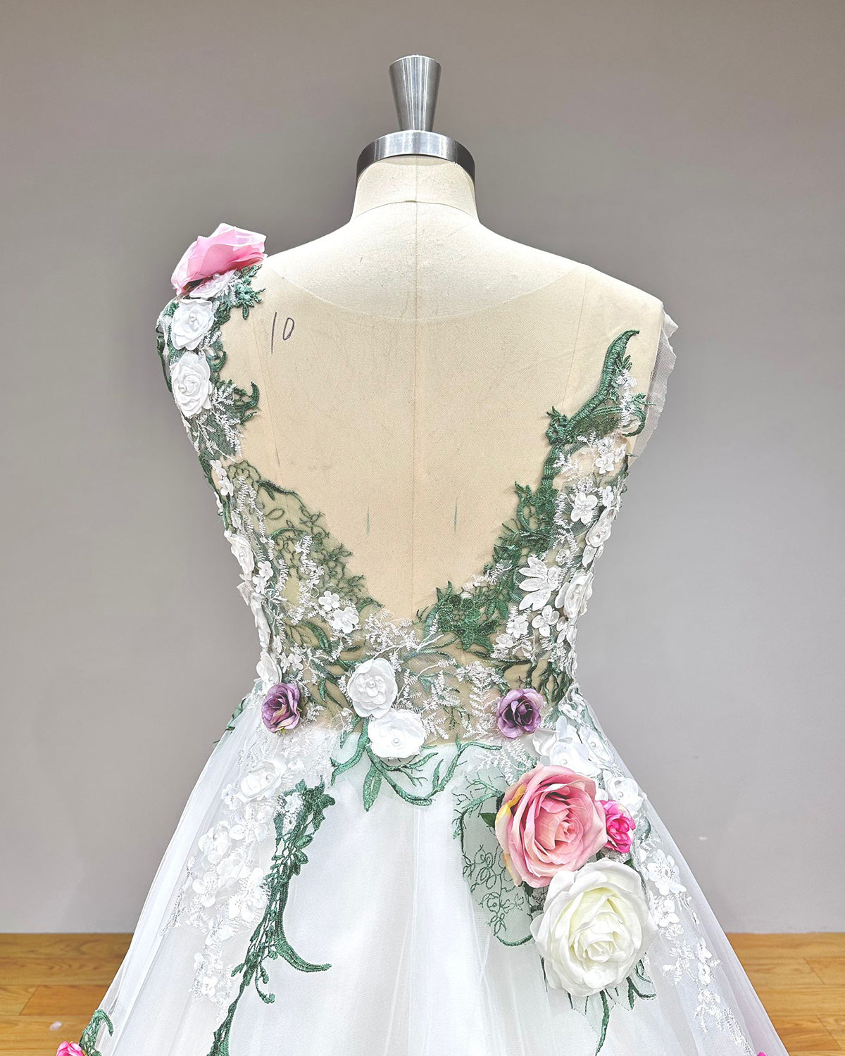 Close-up back bodice detail of a pastoral ball gown wedding dress on a mannequin, emphasizing the intricate handmade flowers, soft tulle fabric, and elegant off-shoulder design.