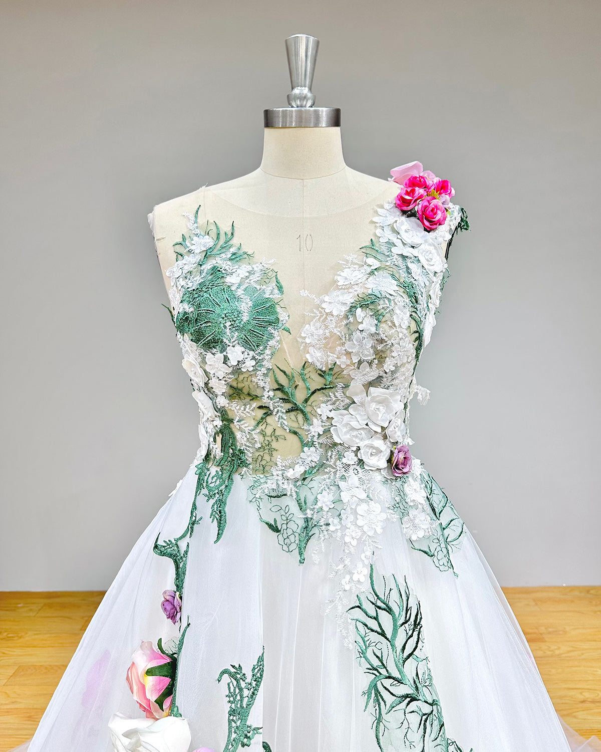Close-up front bodice detail of a pastoral ball gown wedding dress on a mannequin, emphasizing the intricate handmade flowers, soft tulle fabric, and elegant off-shoulder design.