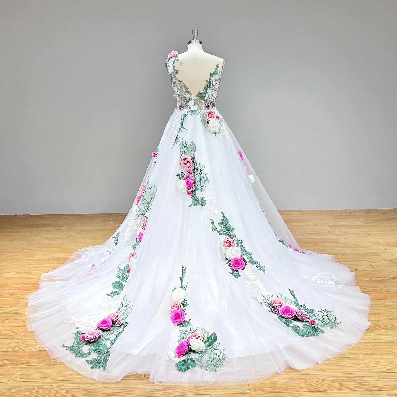 Dramatic back view of a handmade flowers ball gown wedding dress on a mannequin, showcasing the illusion back detailing, delicate lace elements, and a sweeping bridal train.