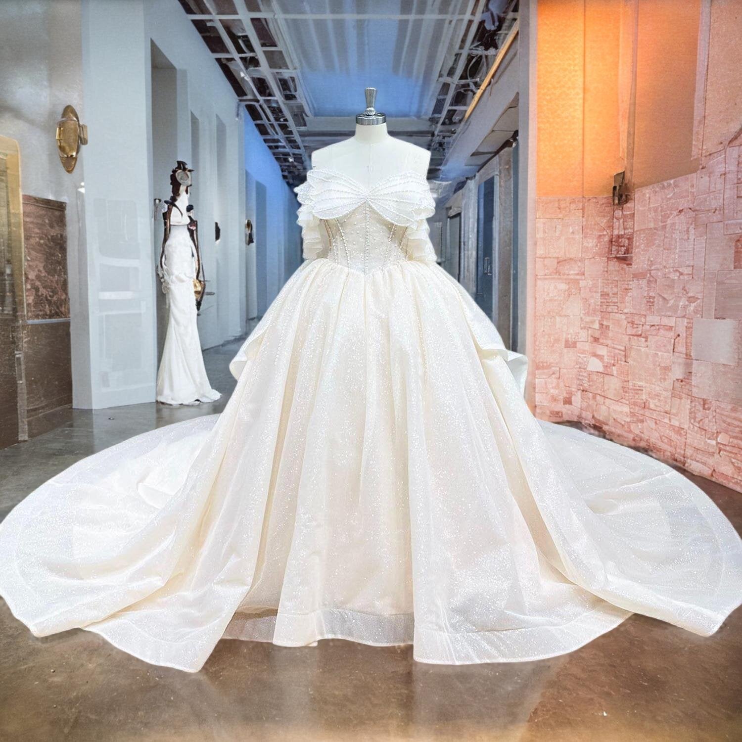Full front view of a pearl bow glitter ball gown wedding dress on a mannequin in a studio hallway, highlighting the exquisite off-shoulder bodice and wide, sparkling tulle train.
