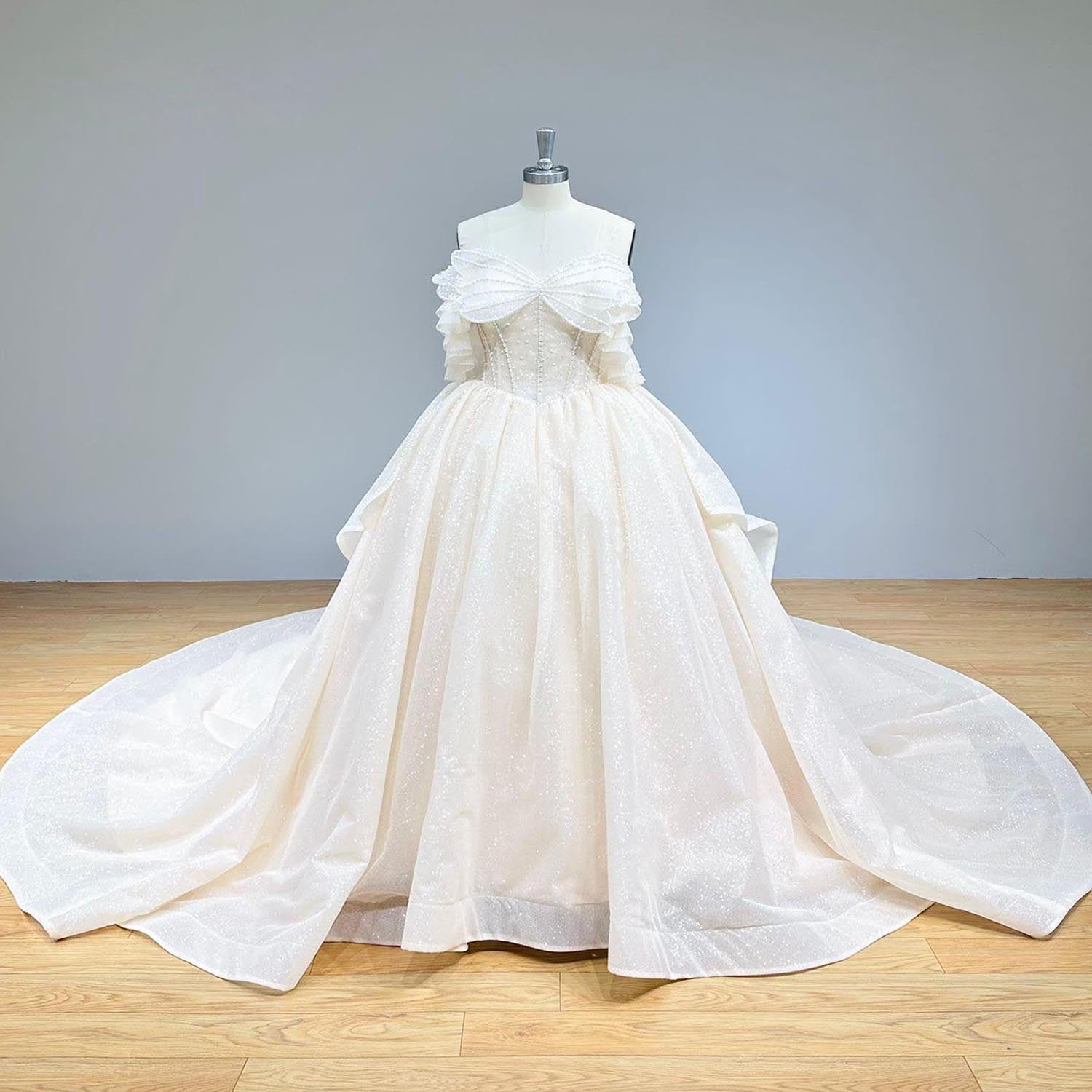 Clean studio front view of a gorgeous pearl bow glitter ball gown wedding dress on a mannequin, emphasizing the off-shoulder neckline and luminous, glittering fabric.