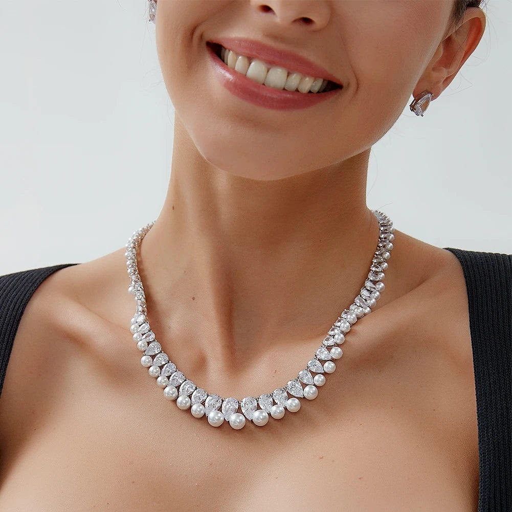 Close-up portrait of a smiling model wearing a luxury pearl choker necklace set with matching teardrop crystal studs.