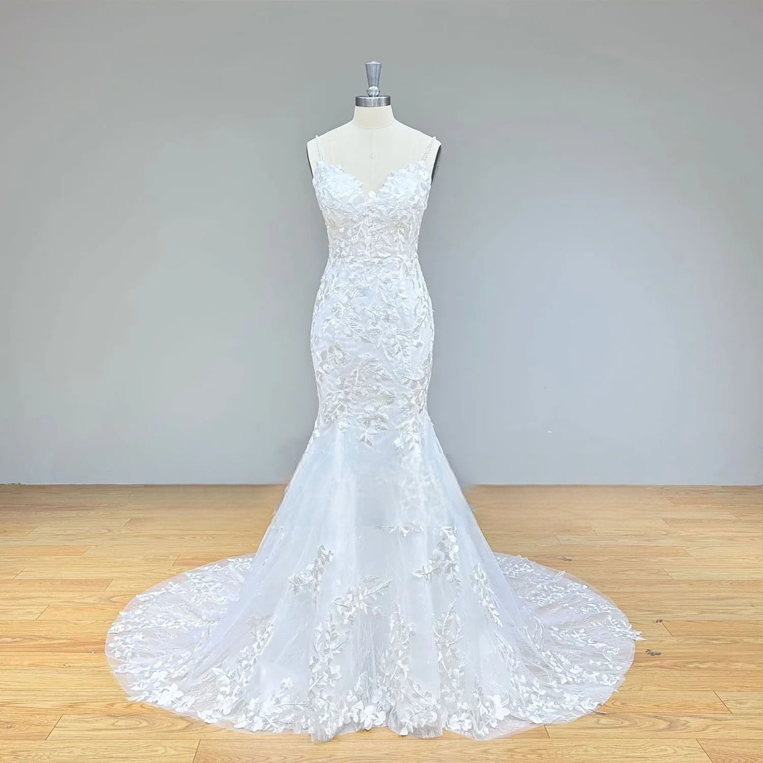 Front view of a form-fitting mermaid bridal dress on a mannequin, featuring thin pearl straps and symmetrical floral lace embroidery.