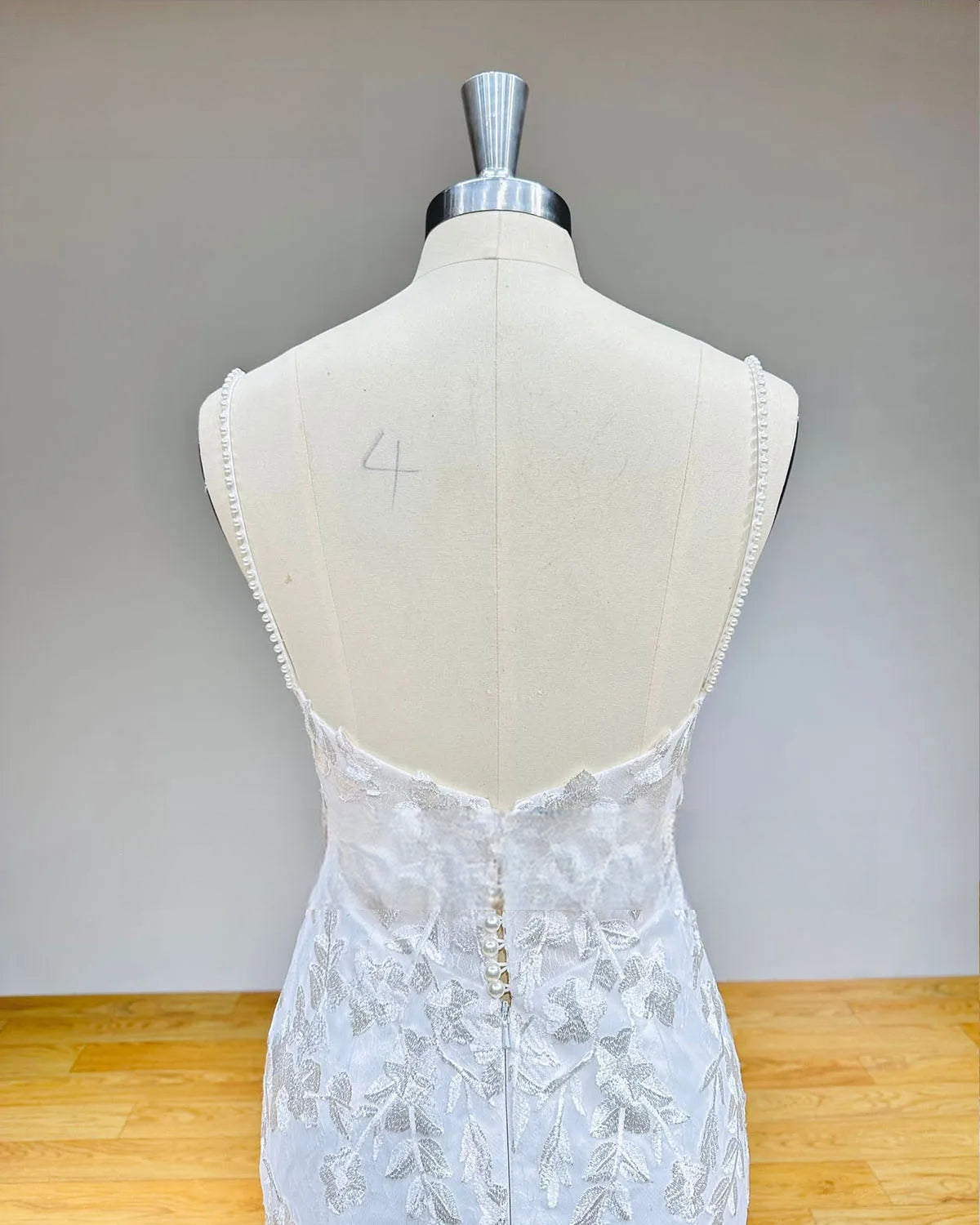 Detailed close-up of a backless wedding dress bodice featuring a row of classic bridal buttons and delicate lace appliques on sheer illusion mesh.