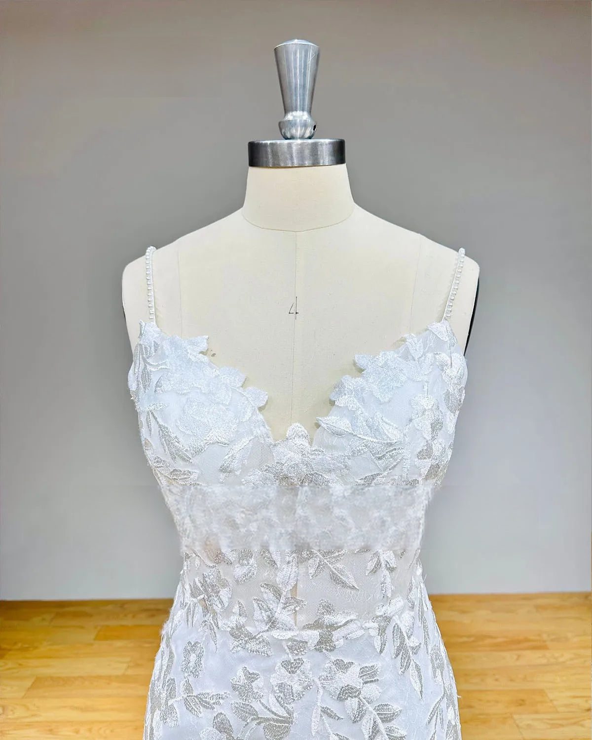 Close-up of a sweetheart neckline bridal bodice with thin pearl-beaded straps and handcrafted floral lace details.