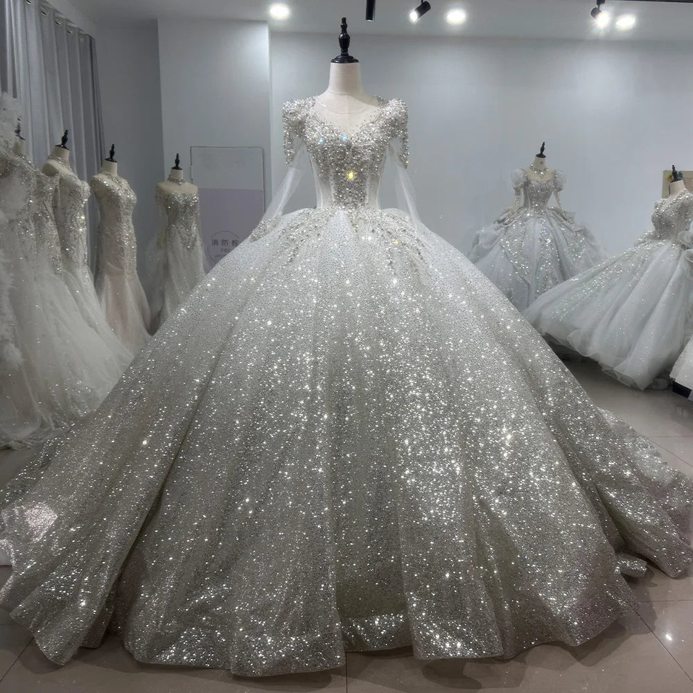 Bride wearing a luxury pearl-embellished long sleeve ball gown wedding dress with an illusion neckline at a romantic outdoor evening ceremony.