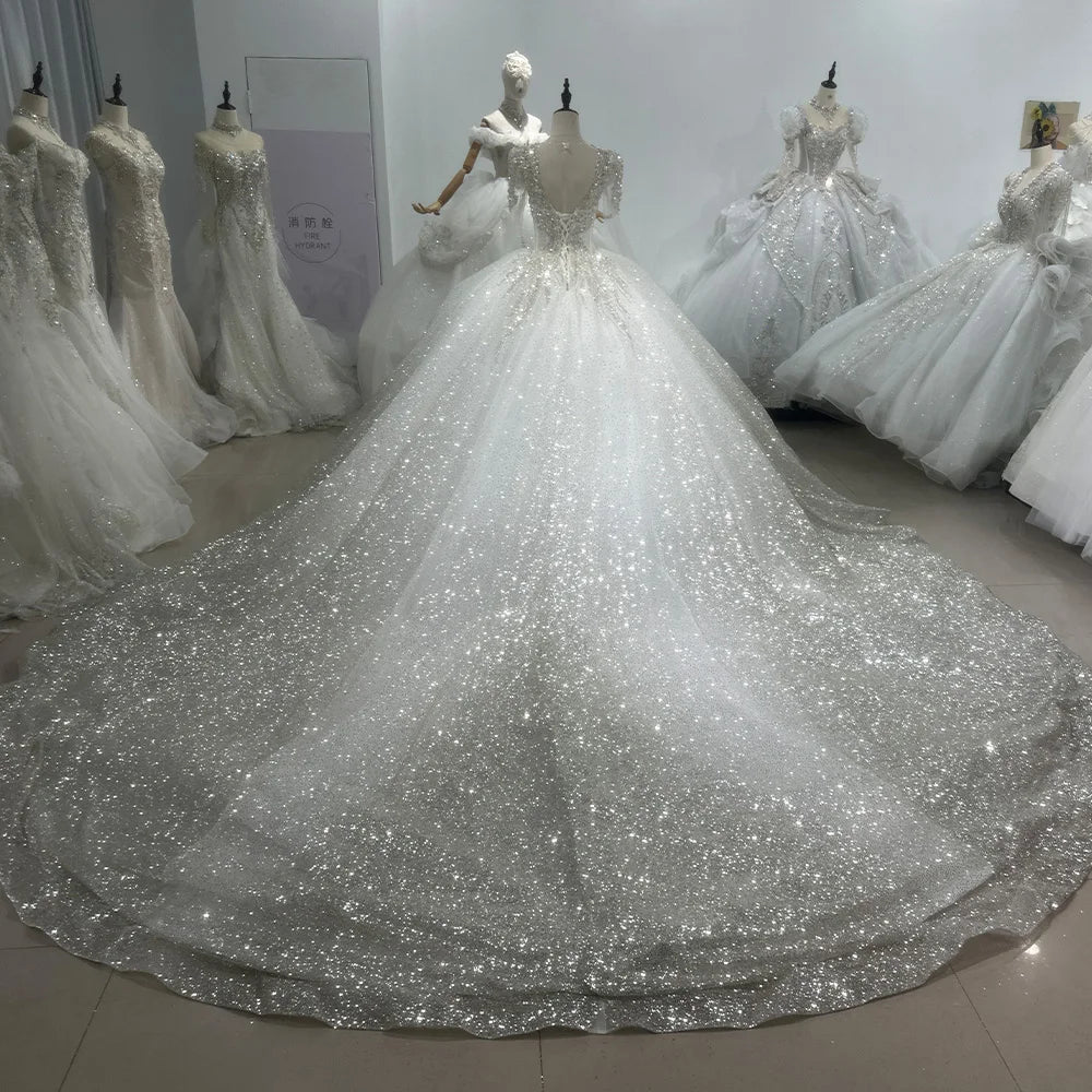 Model showcasing a regal long sleeve pearl bridal gown featuring a structured bodice, deep plunging sweetheart neckline, and a voluminous shimmering tulle skirt.
