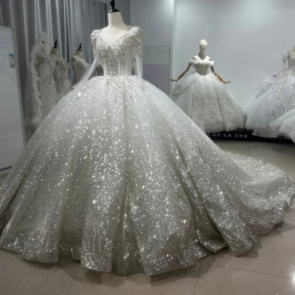 Detailed front close-up of a princess bridal gown bodice, showcasing high-density pearl beading, silver crystal embroidery, and sheer long illusion sleeves.