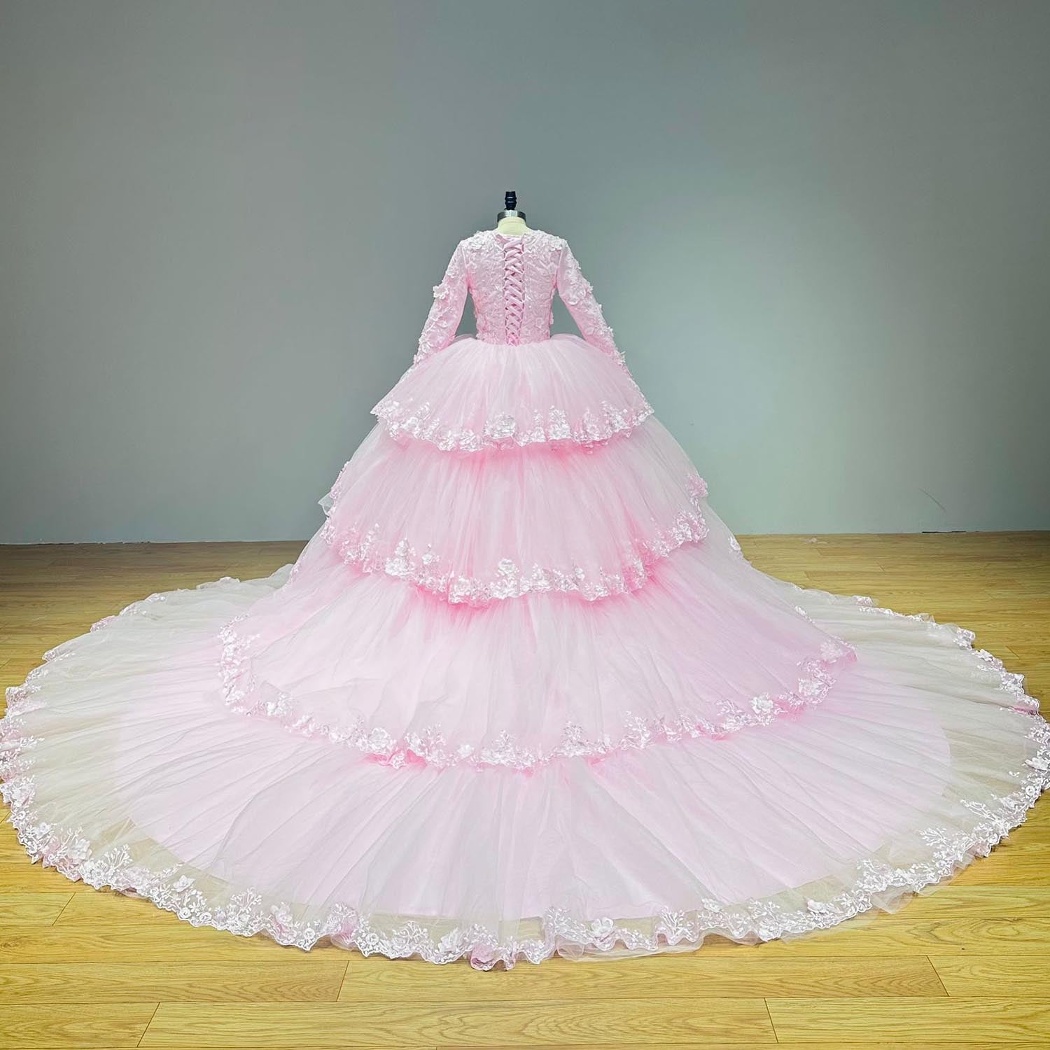Full studio back view of the pink wedding gown featuring the multi-tiered detachable tulle train extension trailing out into a wide scalloped circle.