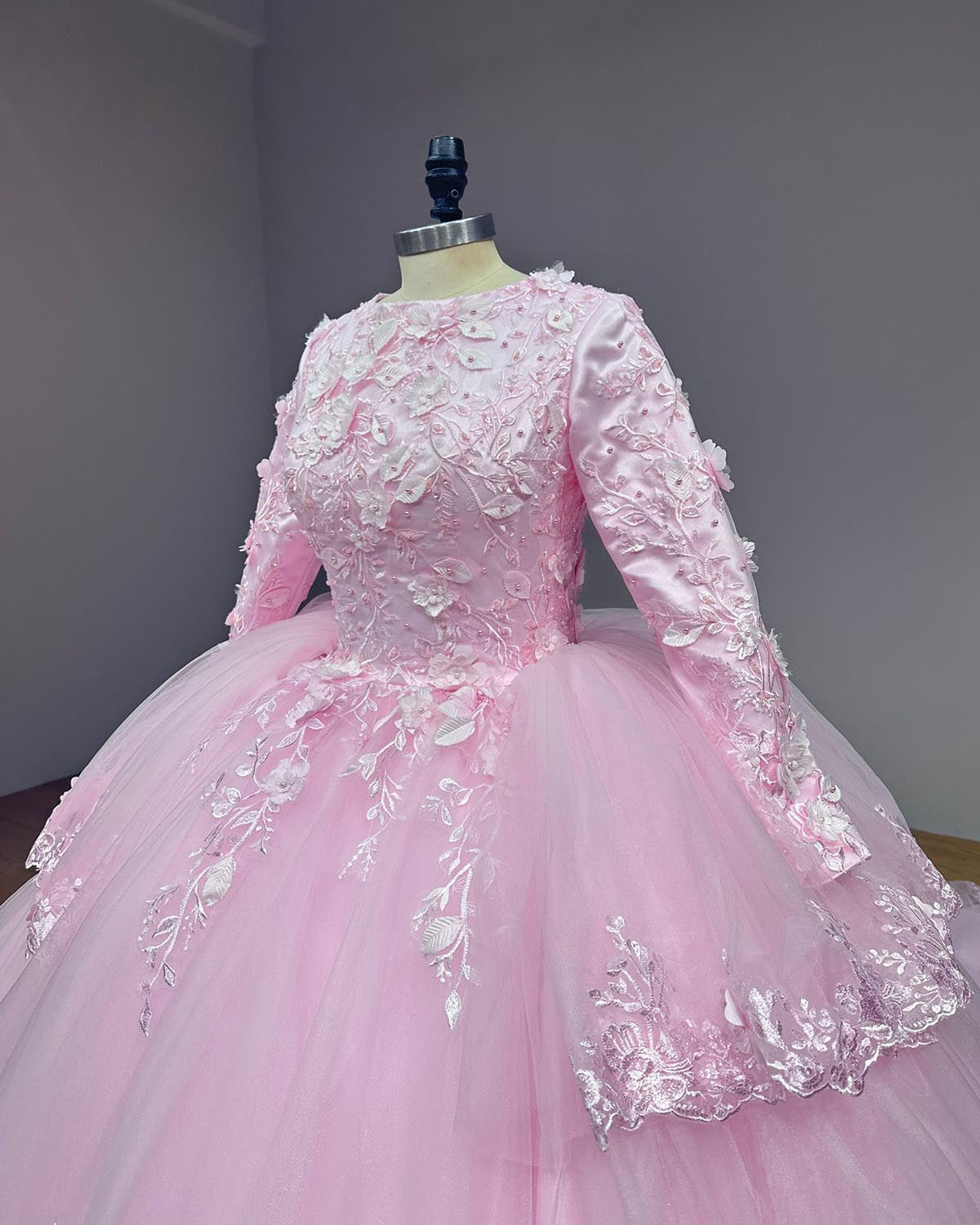 Close-up side perspective of a pink long-sleeve wedding dress bodice highlighting intricate white leaf lace embroidery and dimensional fabric flowers.