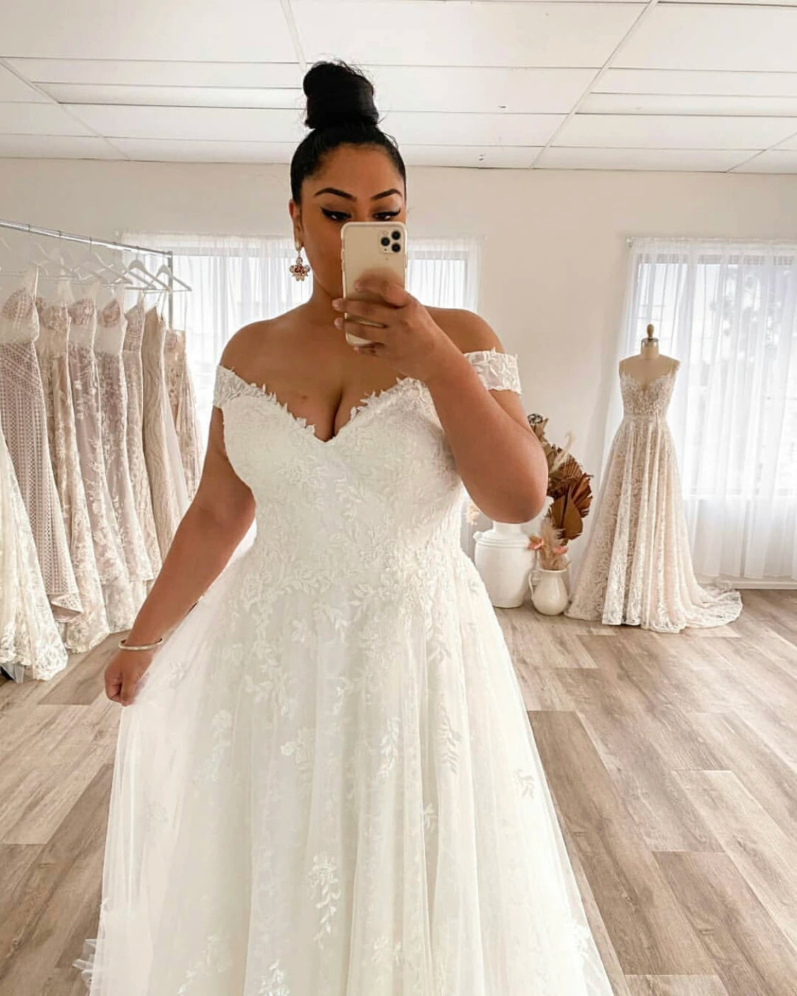 Side view of a plus-size bride wearing a backless bridal gown, highlighting the lace applique and A-line silhouette in a bridal shop mirror.
