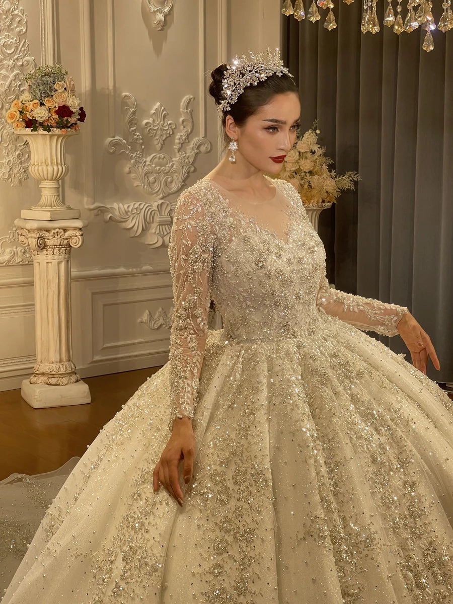 Close-up side view of the sparkly wedding dress bodice highlighting the dense pearl and sequin detailing on the long illusion sleeves and the model wearing a matching royal bridal tiara.