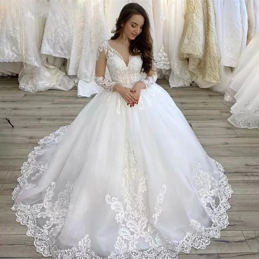 Beautiful bridal gown with a V-neck bodice, long lace sleeves, and a voluminous tulle skirt with a detailed court train.