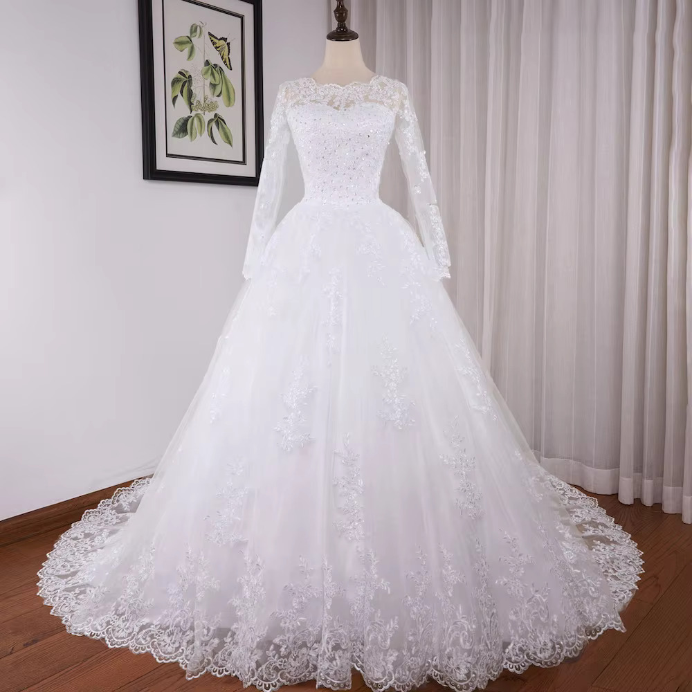 Full-length front view of a bride wearing a regal princess ball gown wedding dress with elegant long sheer lace sleeves, a structured neckline, and a voluminous sparkling tulle skirt.