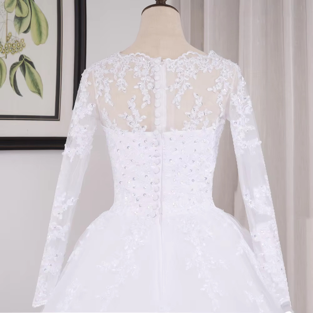 Rear view of the long sleeve plus size bridal gown, showcasing an intricate sheer lace illusion back with button closures and a sweeping, dramatic cathedral-length ball gown train.