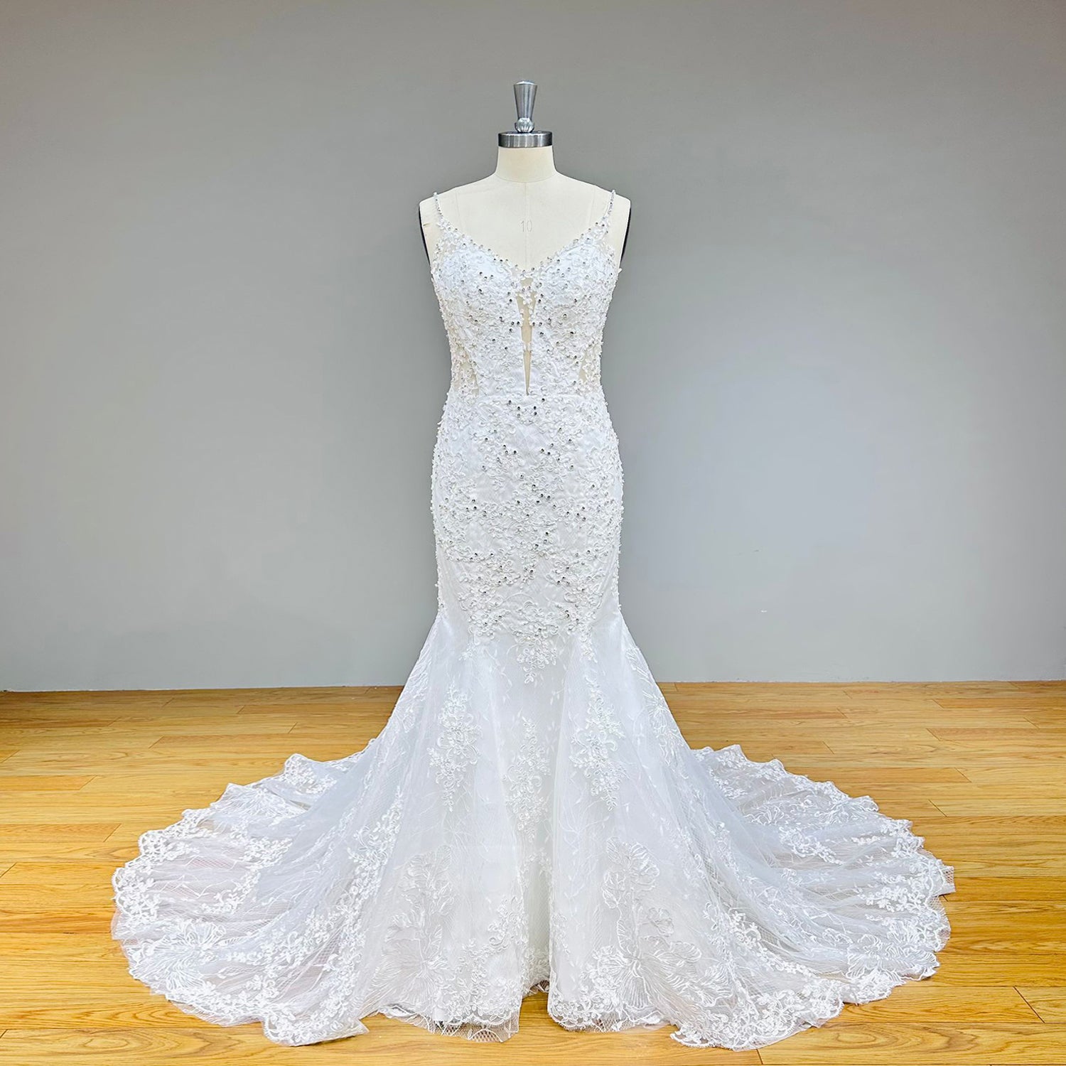 Front view of a crystal-beaded mermaid wedding dress with delicate beaded straps, structured boning panels, and a scalloped lace hemline on a dress form.