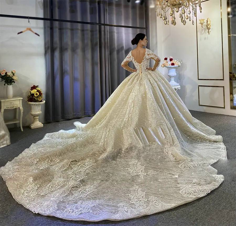 Back view of a stunning bride wearing an elegant princess puffy ball gown wedding dress with long sleeves, showcasing a traditional corset lace-up and a grand, sprawling cathedral train.