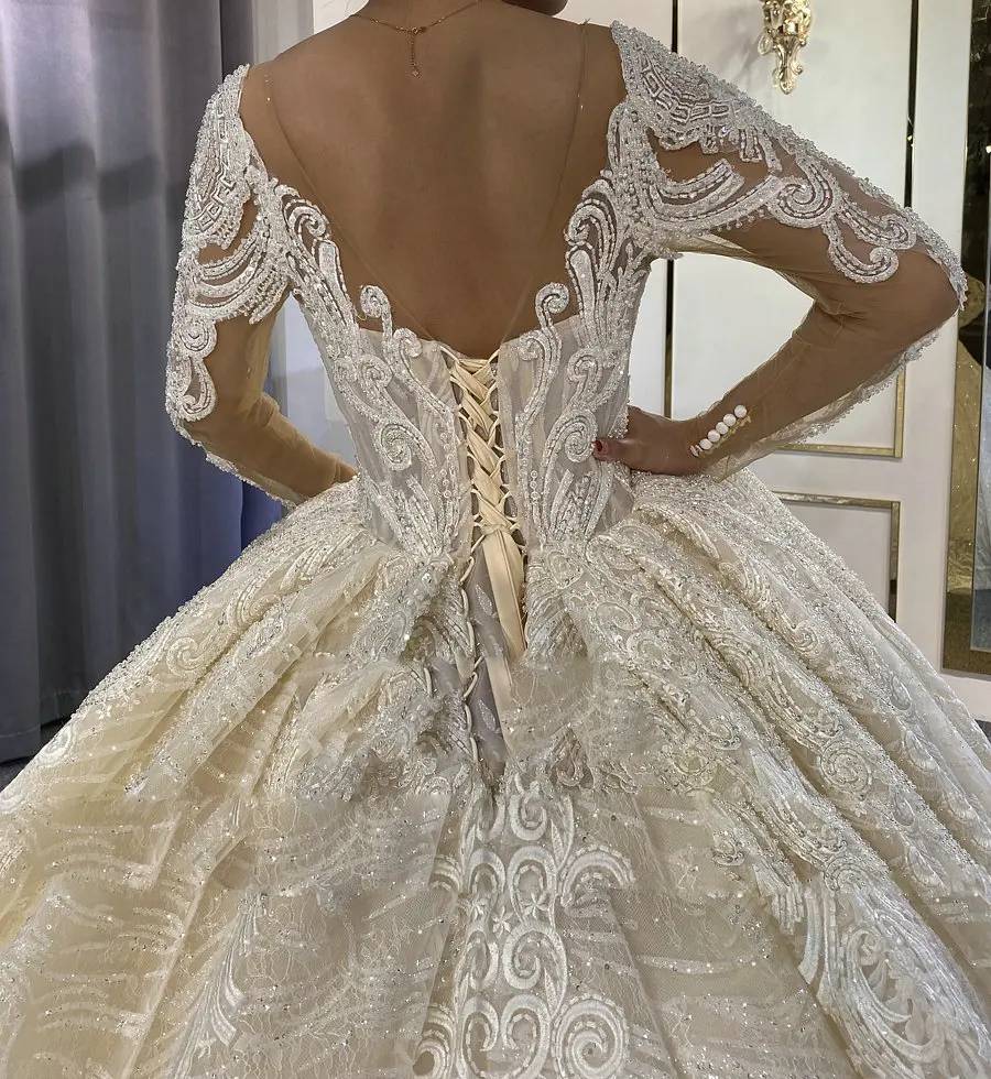 Close-up detail of the open back on a long-sleeved elegant bridal ball gown, featuring a classic lace-up corset design and intricate beaded lace appliqués.