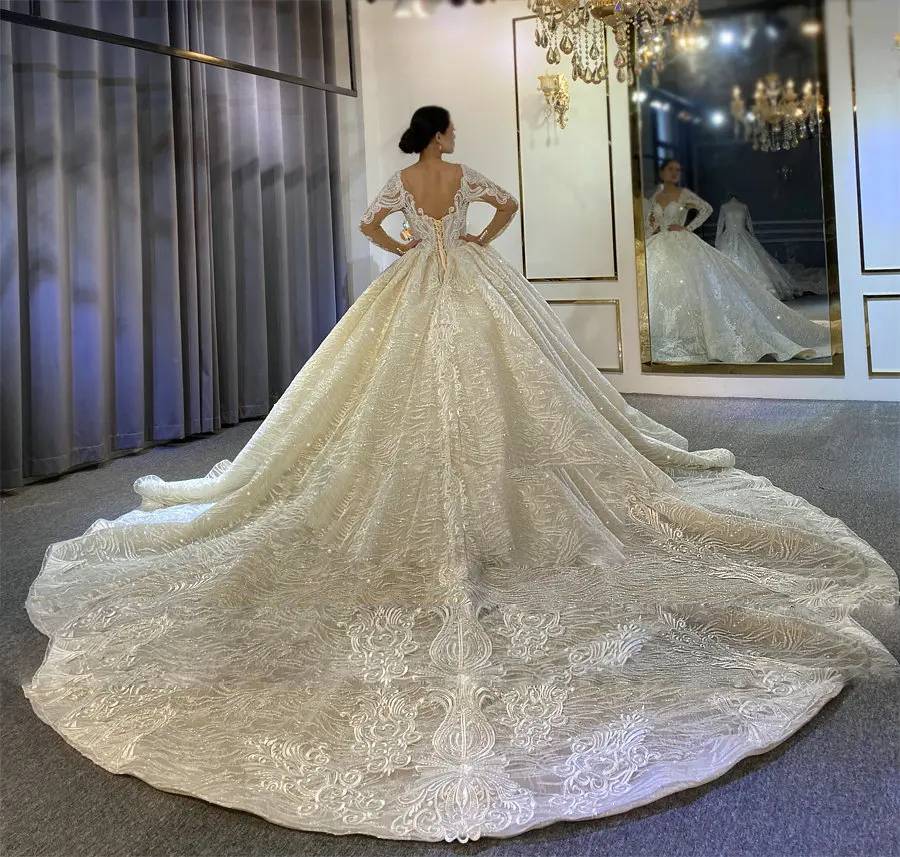 Rear perspective of a model in a bridal boutique displaying the massive, shimmering circular train of an elegant princess puffy ball gown wedding dress.