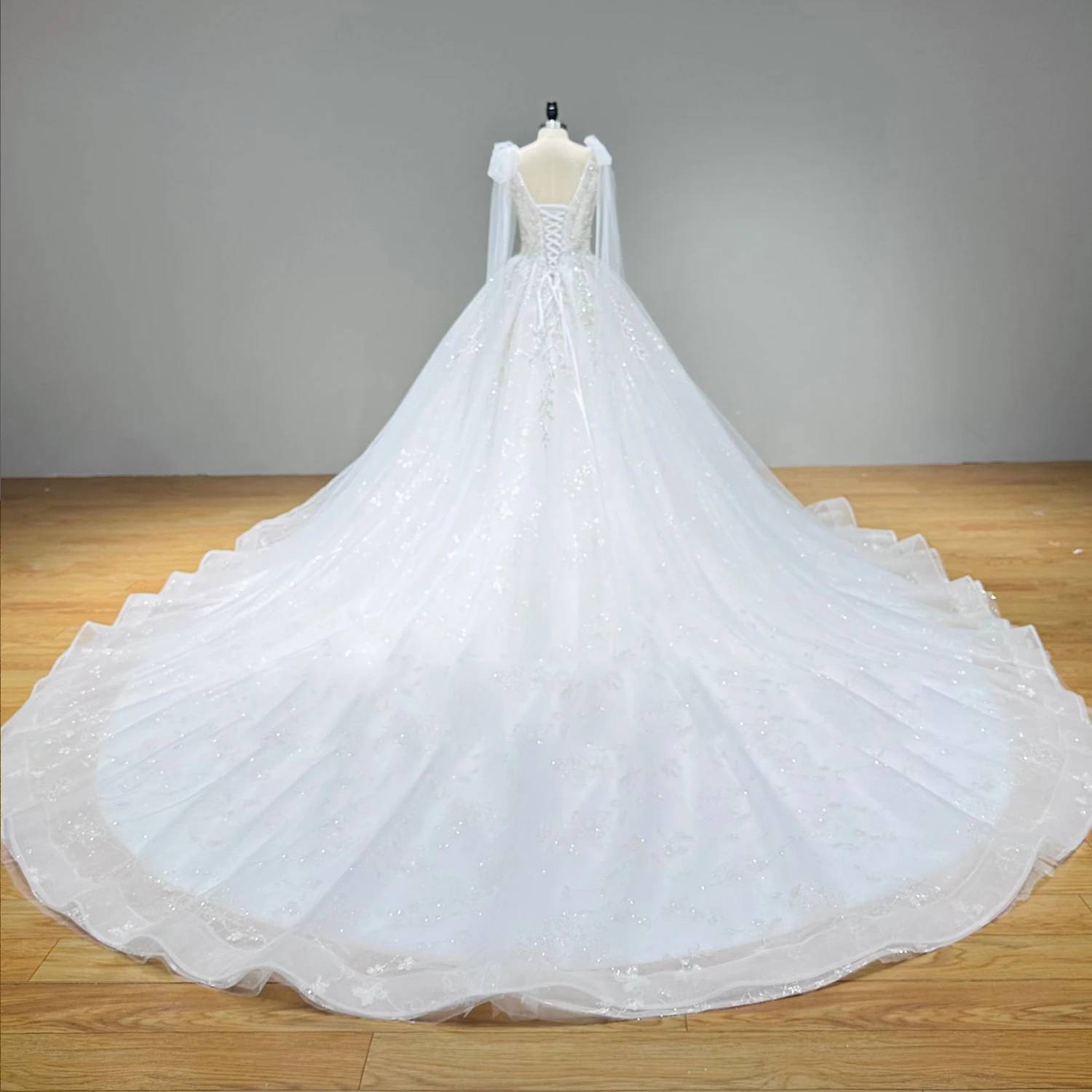 Full back view of an ivory ball gown wedding dress on a mannequin displaying a classic lace-up corset back and an expansive, shimmering sequined chapel-length tulle train.