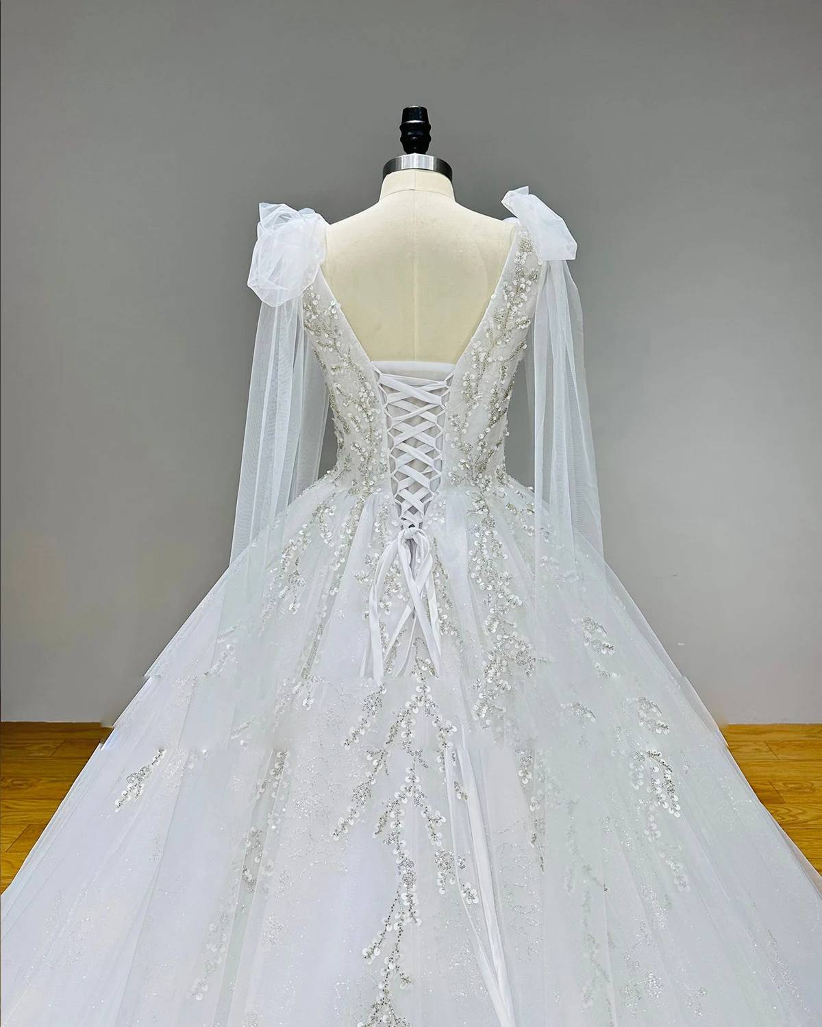 Close-up back details of a bridal ball gown showing the adjustable lace-up corset closure, delicate silver vine embroidery, and sheer tulle shoulder streamers.