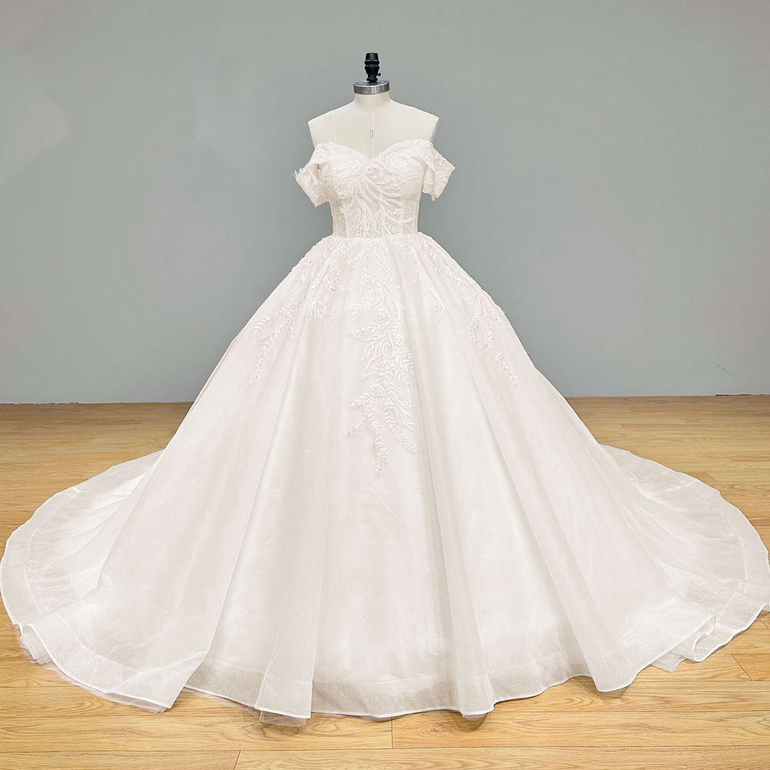 Full front studio view of a high-quality white off-the-shoulder princess ball gown wedding dress featuring trailing leaf sequins on a studio mannequin.
