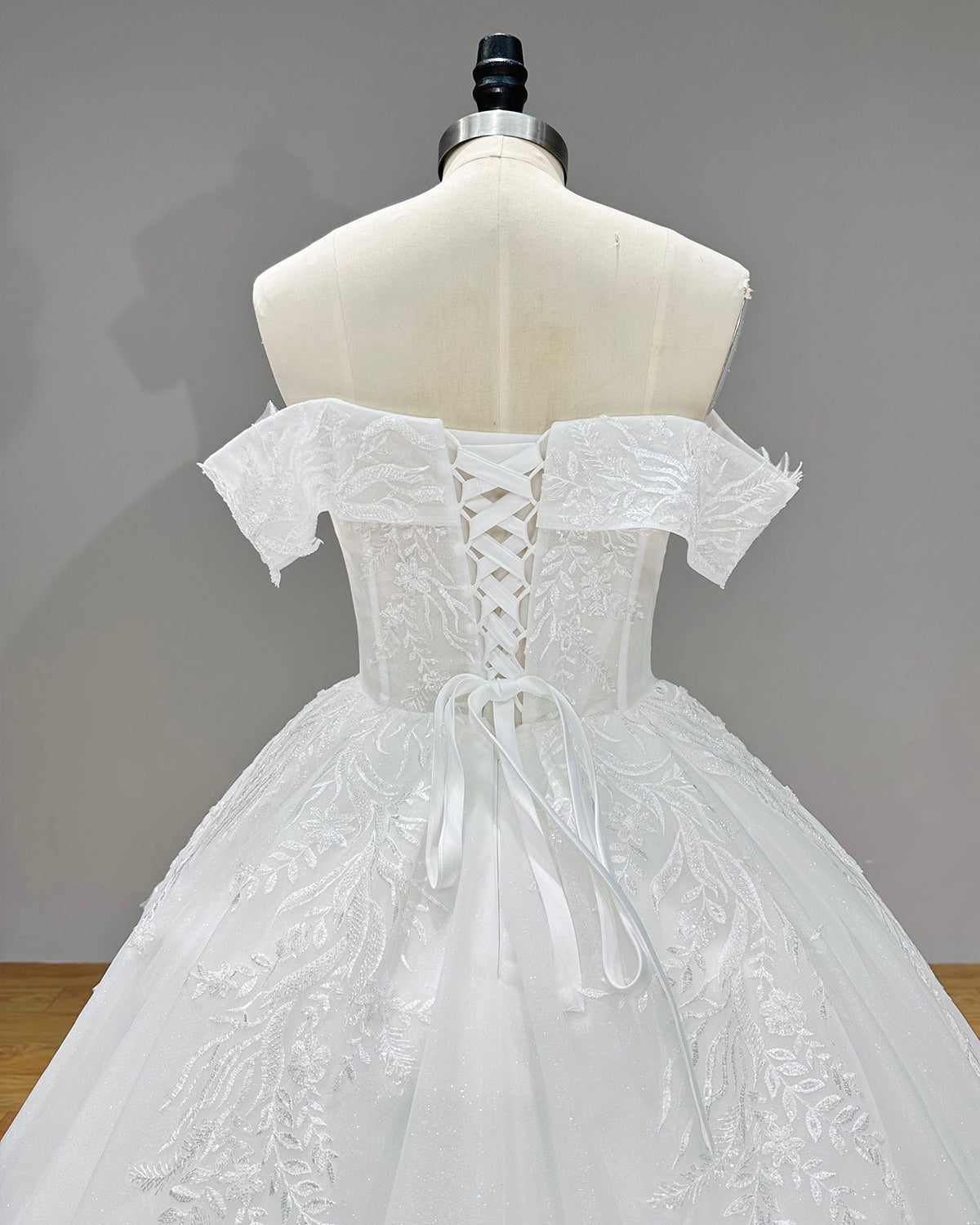 Detailed back view of a white ball gown bodice showing the adjustable ribbon lace-up corset back closure and sheer embroidered leaf lace panels.