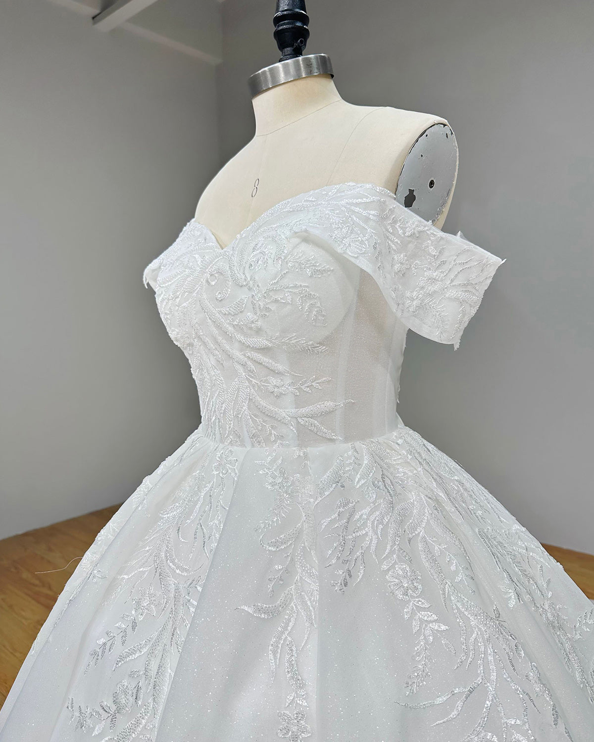 Close-up side profile view of an off-the-shoulder bridal bodice highlighting structured corset boning and delicate leaf-embroidered lace motifs.