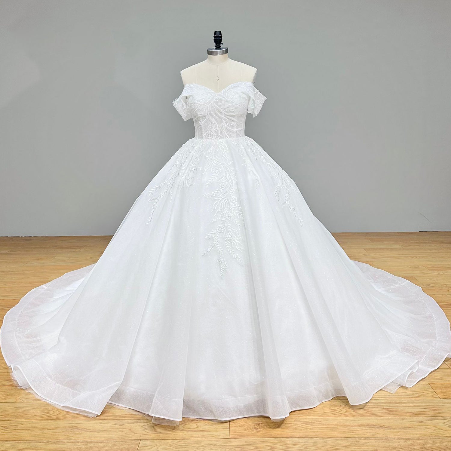 Studio front view of a majestic white shimmer tulle princess wedding gown with a deep sweetheart neckline and trailing leaf appliques on a dress form.