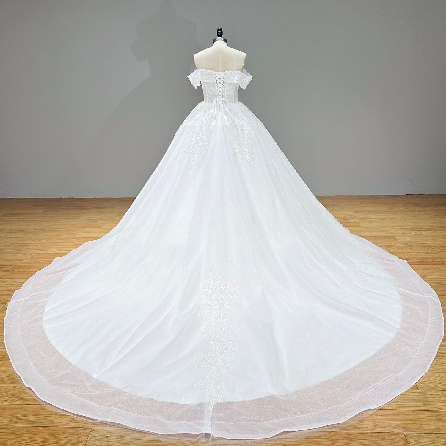 Full-length back studio view of a white princess bridal gown on a mannequin, showcasing an expansive circular cathedral train with a central lace trim.