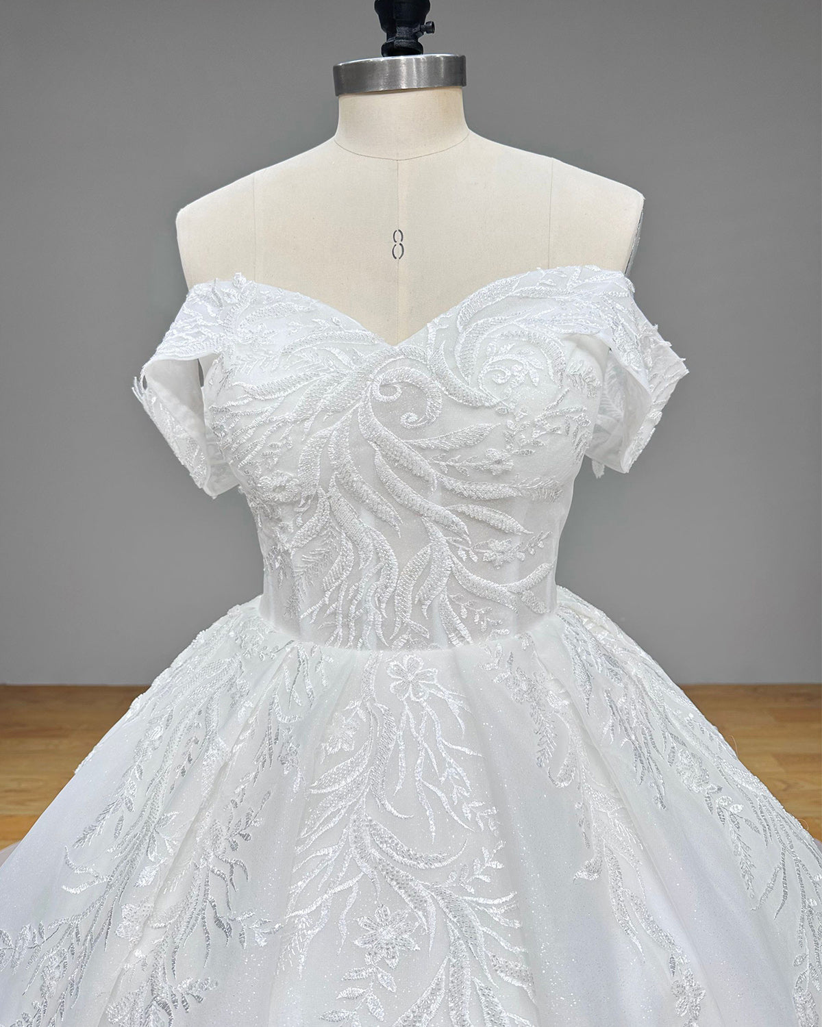 Front close-up of a sweetheart bridal bodice highlighting intricate vine-like leaf embroidery, shimmering sequins, and fine bead clusters.