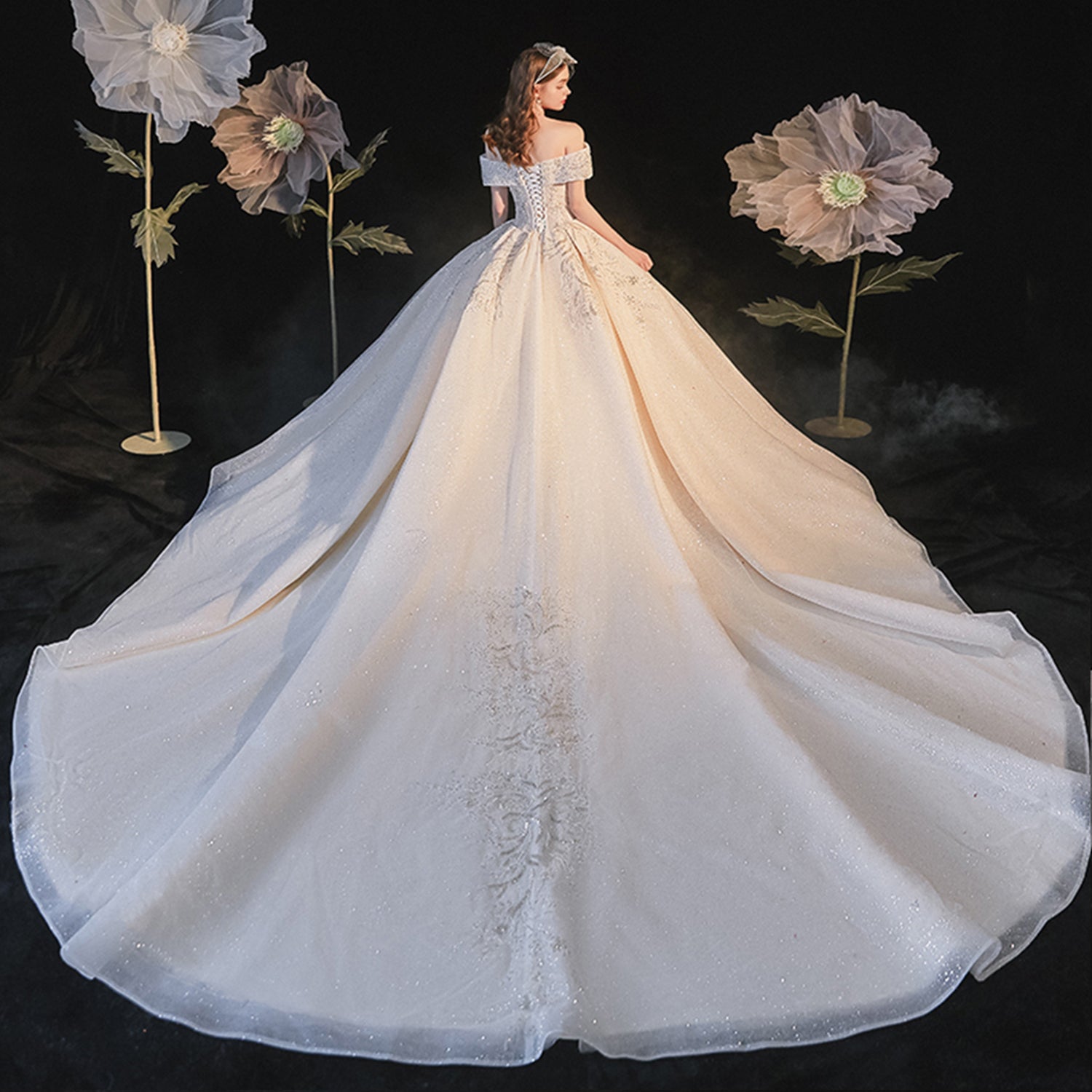 Editorial back view of a model wearing a spectacular champagne glitter tulle ball gown wedding dress showcasing an extra-long cathedral train.