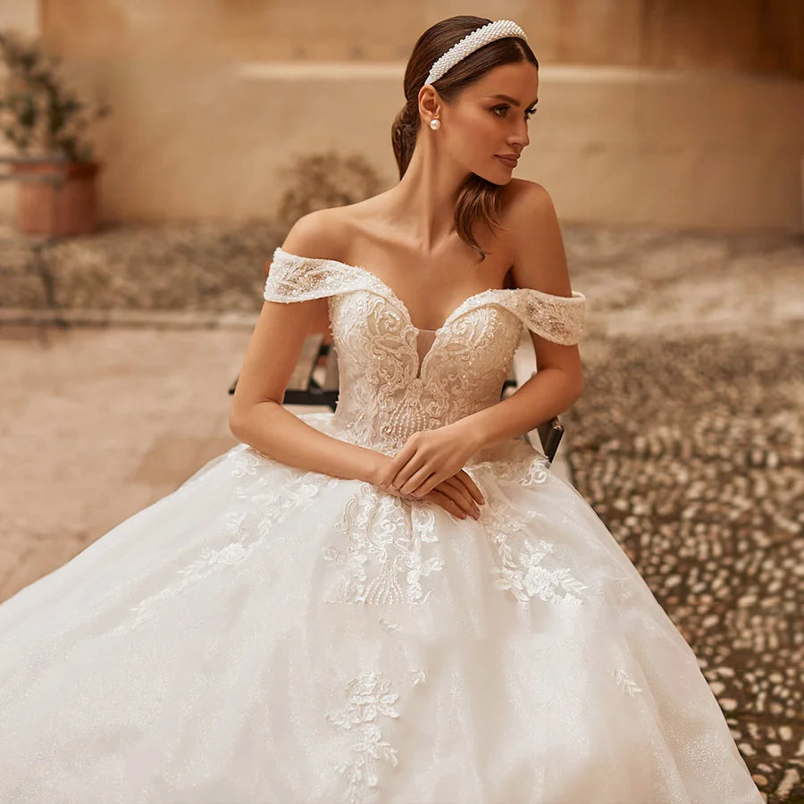 A portrait of a bride modeling a fairy-style ball gown with off-the-shoulder sleeves and romantic floral embroidery.