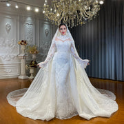 Full-length front view of a luxury 2-in-1 lace mermaid wedding dress with its voluminous removable skirt attached, showcasing a sheer high neck, long sleeves, and a matching bridal veil.
