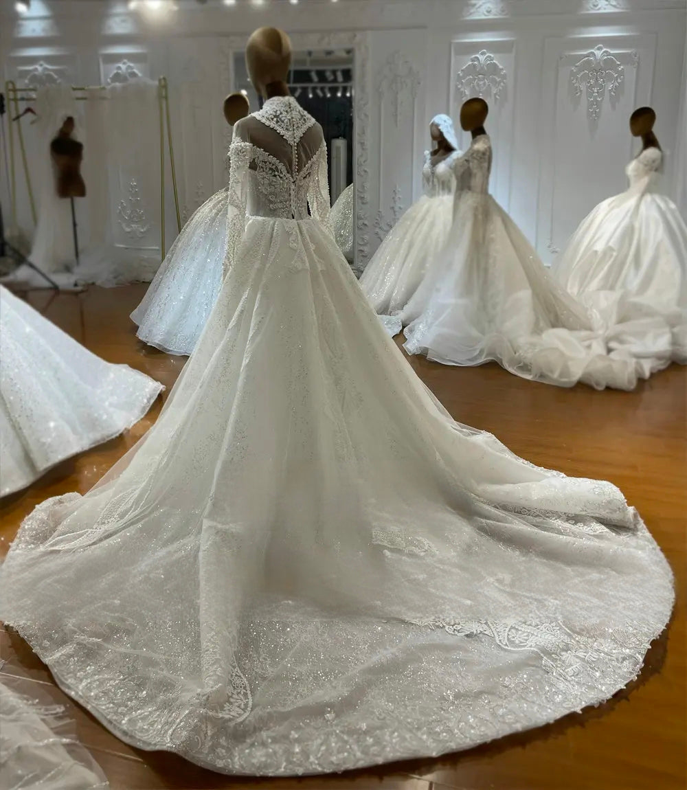 Rear view of a convertible 2-in-1 lace wedding dress on a mannequin, highlighting the attached removable overskirt that creates a dramatic ball gown silhouette with a shimmering long cathedral train.