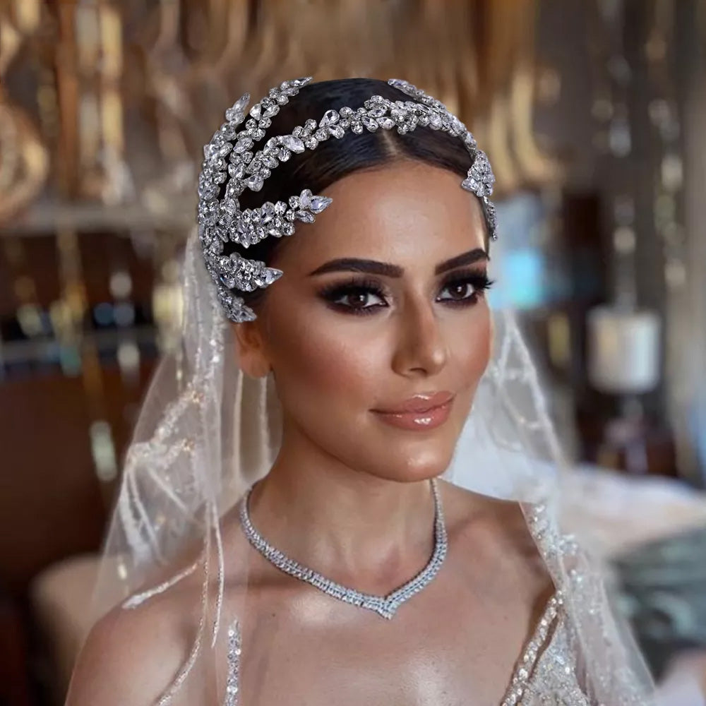 Close-up portrait of a bride with a wedding veil wearing an elegant rhinestone bridal headpiece featuring a curved silver leaf branch pattern.