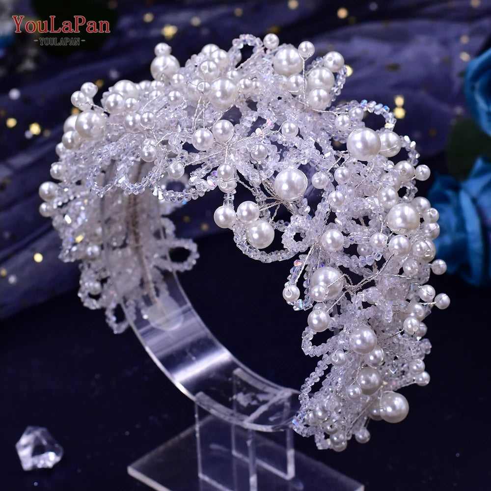 Glamorous multi-layered wedding statement headpiece heavily woven with clear glass crystals and round white pearls on a clear stand.