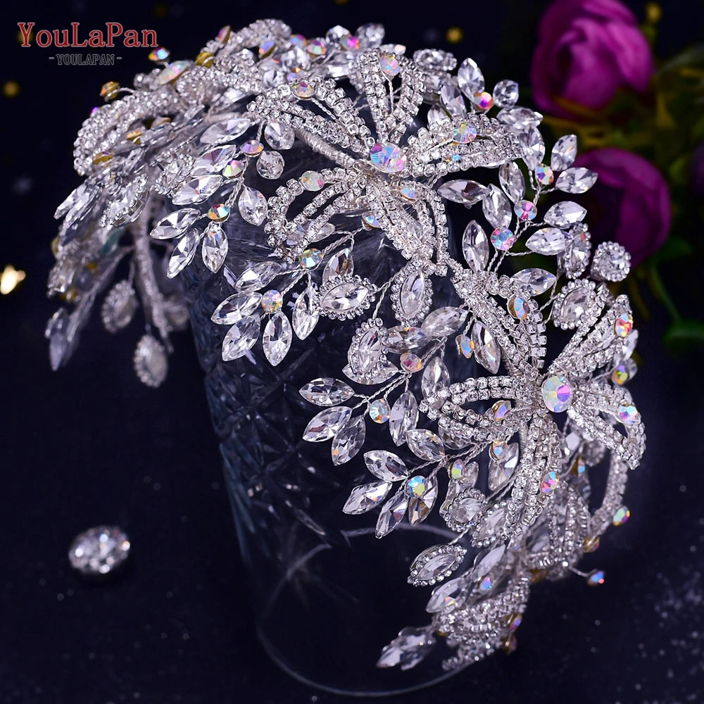 Top-down studio shot of an oversized luxury crystal bridal hair vine with prominent floral clusters, resting over a dark background next to purple roses.