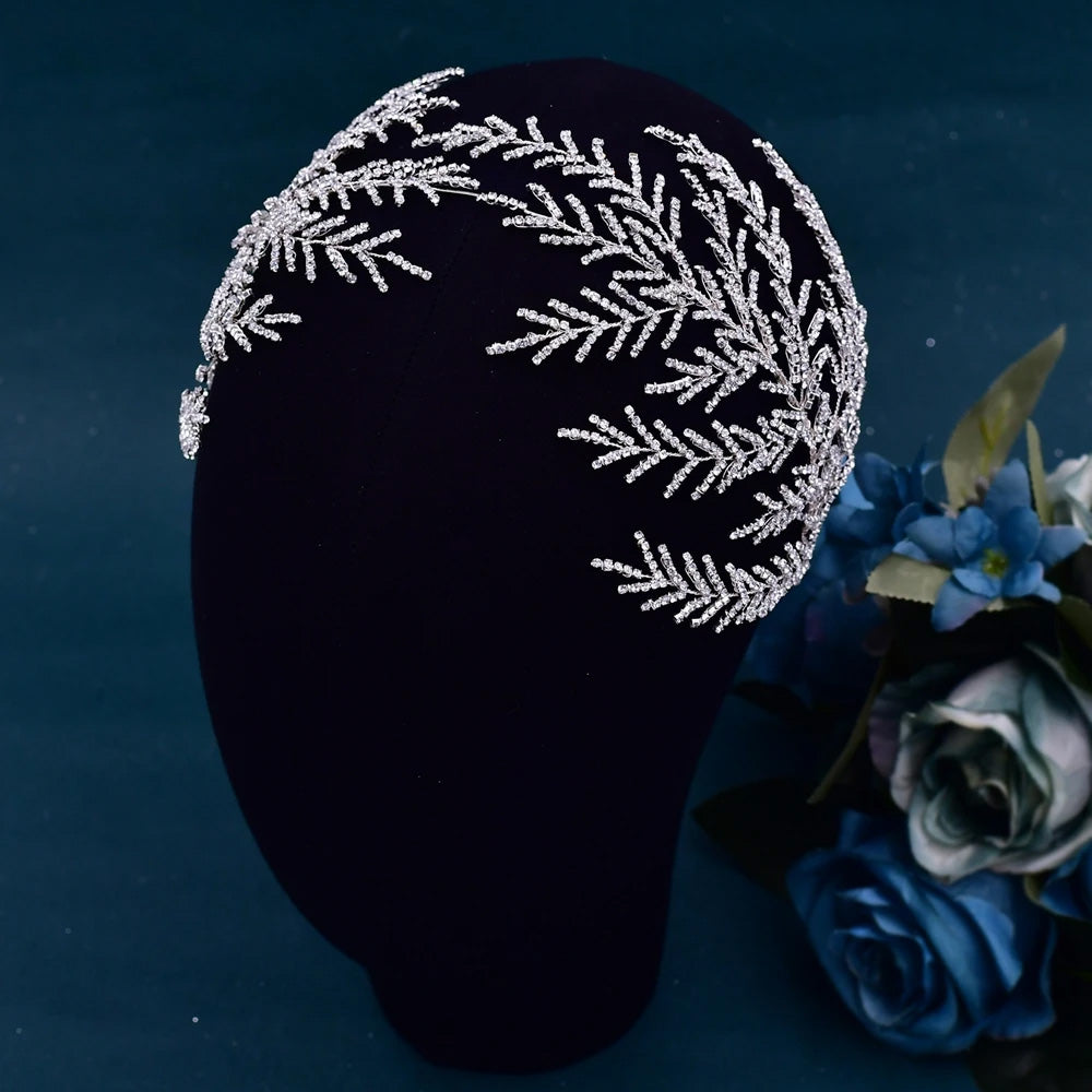 Asymmetric crystal leaf bridal headband with a dense pave rhinestone pine branch structure displayed on a black mannequin profile.