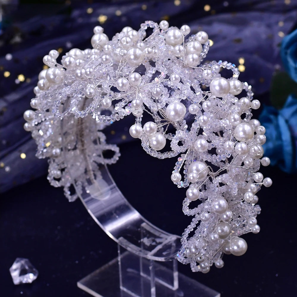 Glamorous multi-layered wedding statement headpiece heavily woven with shimmering glass crystals and round white pearls on a clear stand.