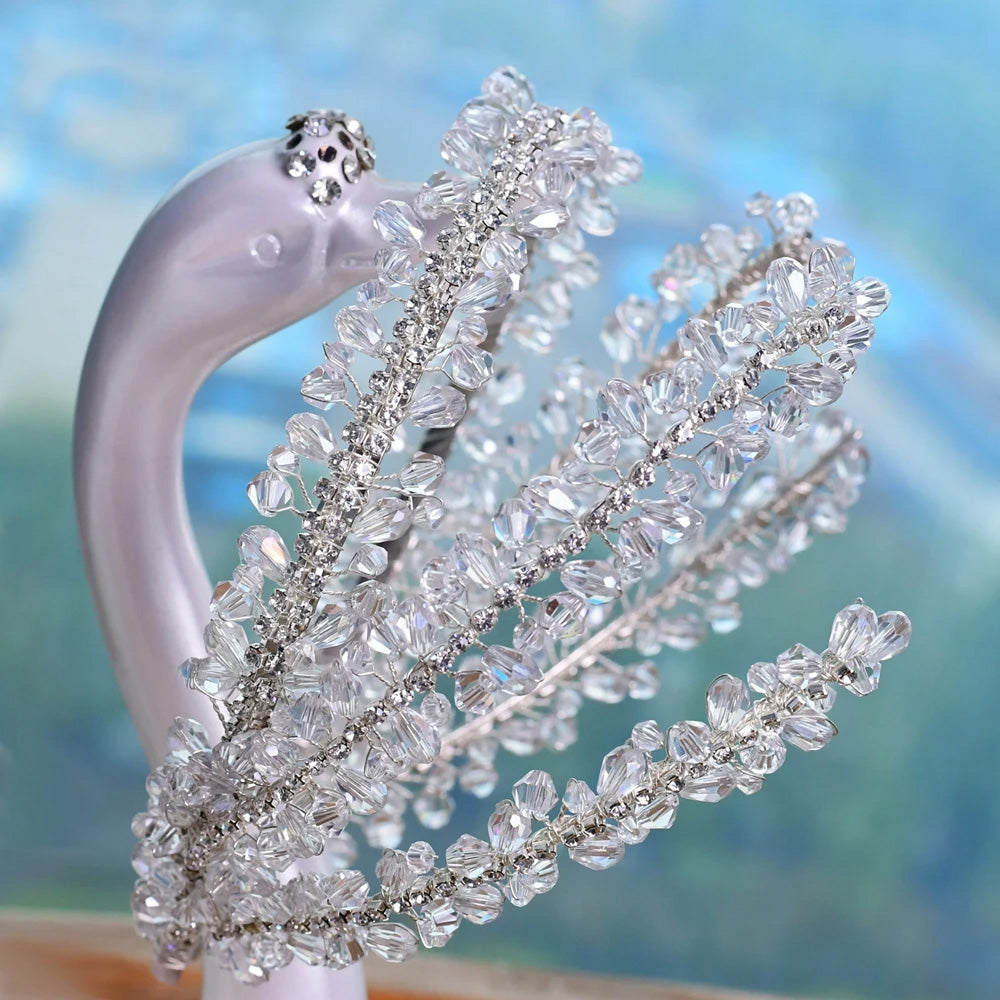 Close-up macro photograph highlighting the detailed gemstone clusters and fine wirework on a glamorous silver wedding hair accessory draped on a porcelain swan figurine.