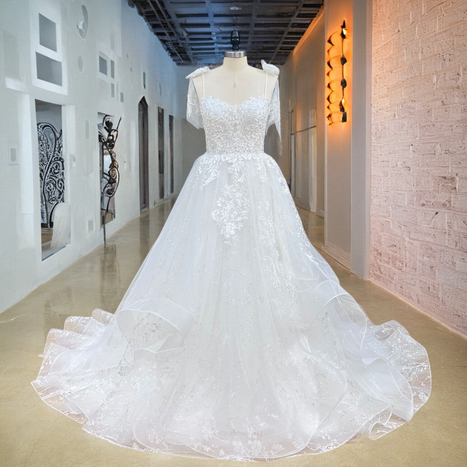 Full front view of a sleeveless sweetheart A-line wedding dress on a mannequin in a bright hallway, highlighting the thin spaghetti straps and layered tulle skirt.