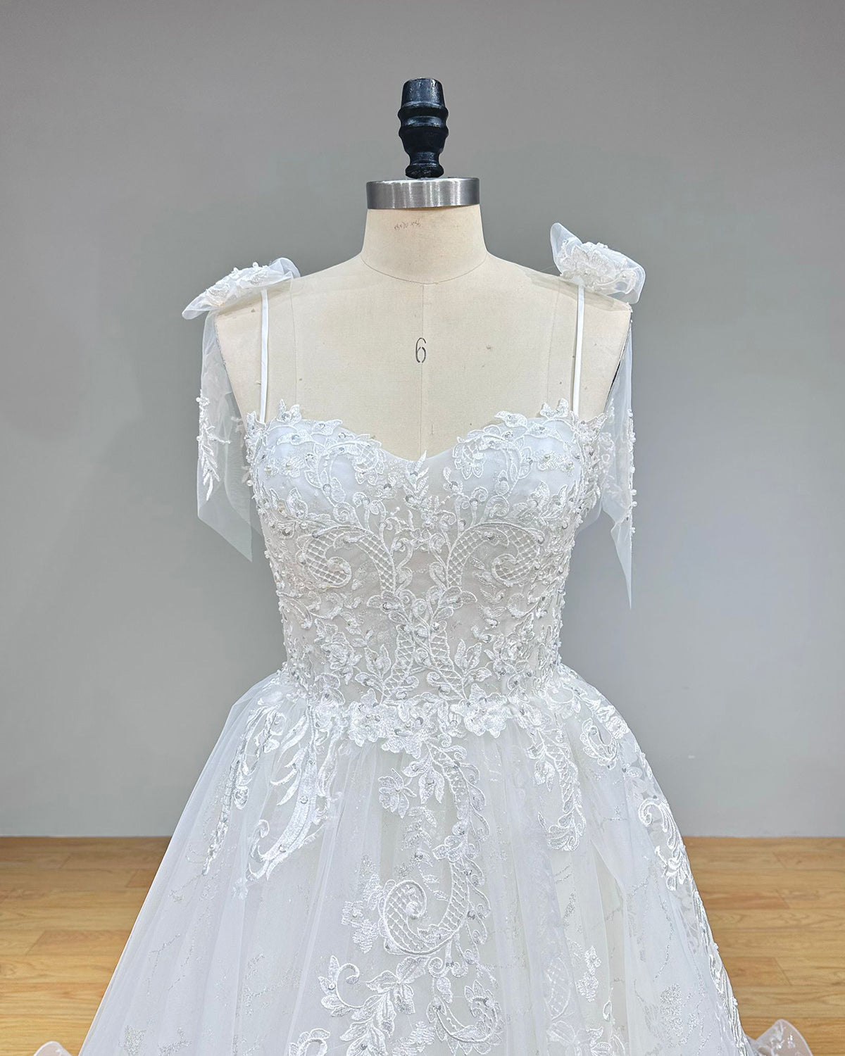 Close-up front bodice detail of a sleeveless wedding gown on a mannequin, emphasizing the sweetheart neckline, delicate lace appliques, and thin spaghetti straps.