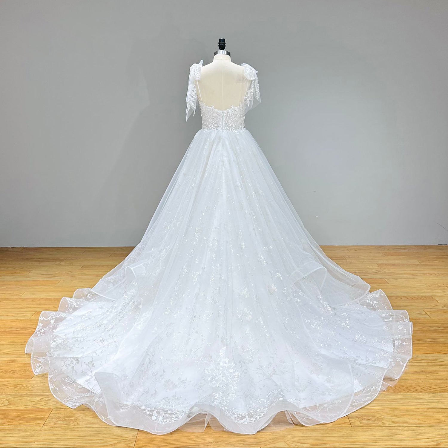 Wide back view of a robe marriage sweetheart wedding gown on a mannequin, showcasing the exquisite lace-up back closure and a long train spreading across a wooden studio floor.