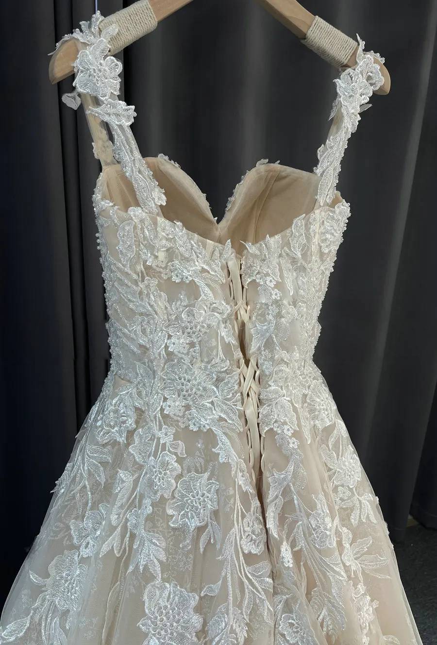Close-up of the back of the romantic A-line lace wedding dress, highlighting the corset tie closure and floral lace details.