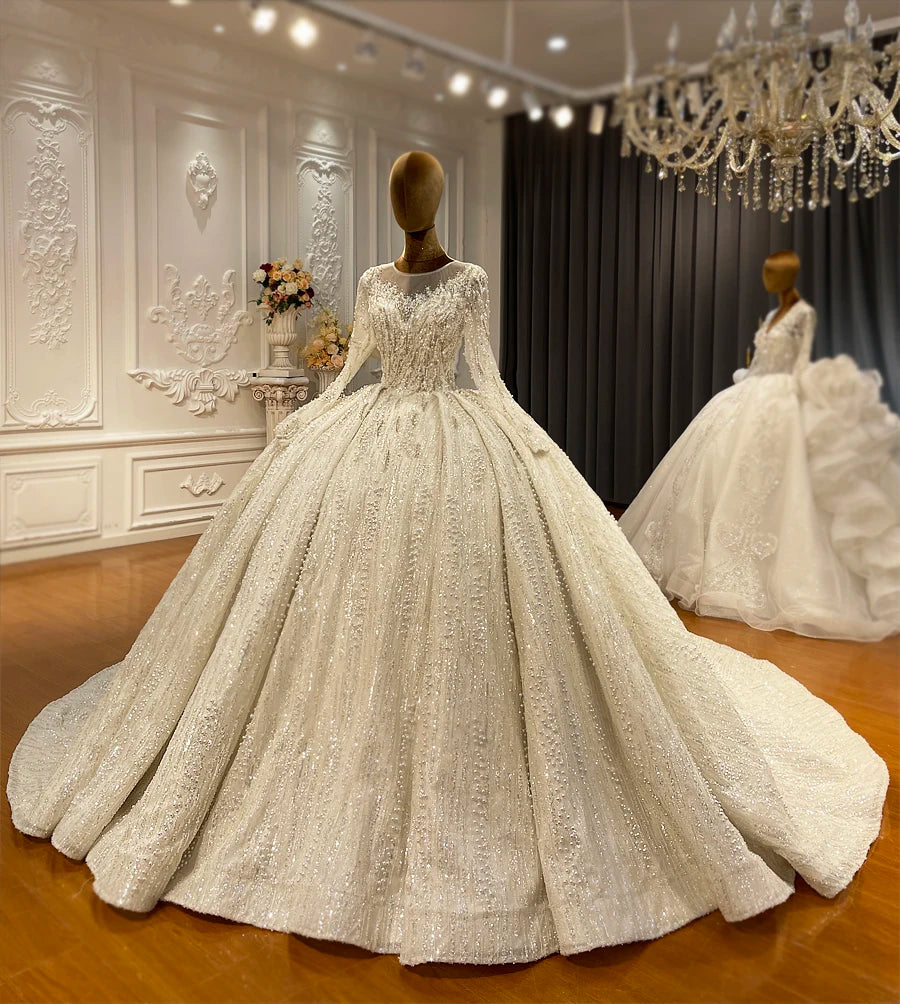 Close-up of the bodice on a romantic long sleeve wedding dress on a mannequin, showcasing the heavy, intricate pearl and crystal beading on a sheer high neckline.
